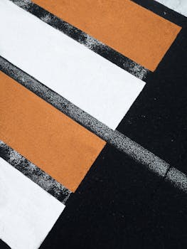 Photo by Igor Haritanovich Detailed view of a colorful pedestrian crossing with orange and white stripes on asphalt.
