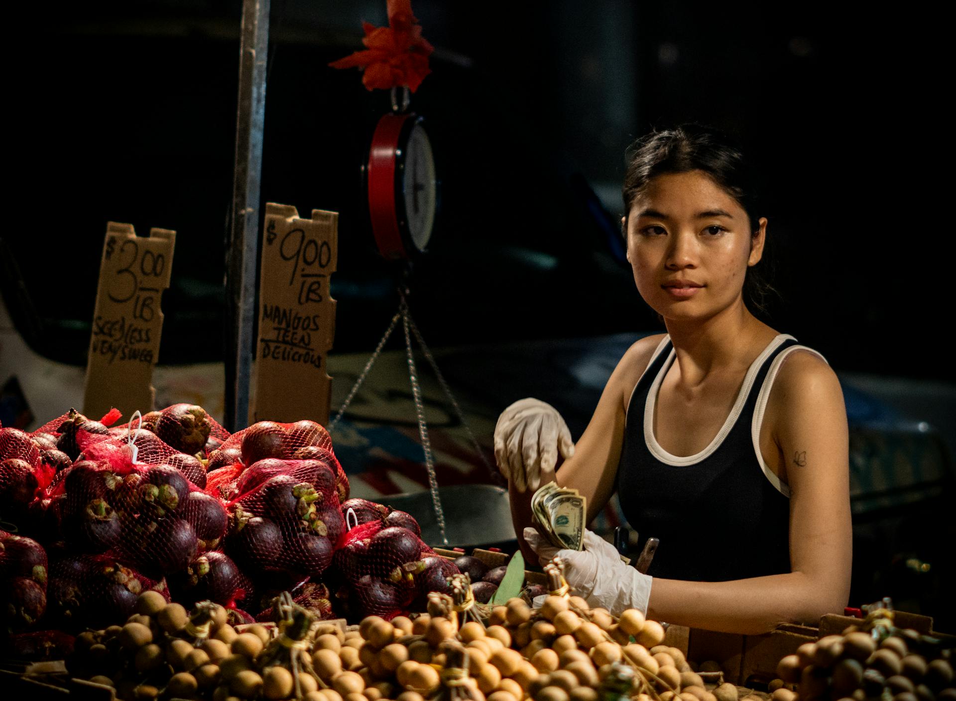 A Woman Sitting at a Food Stall at a Market and Holding Money in Her Hand