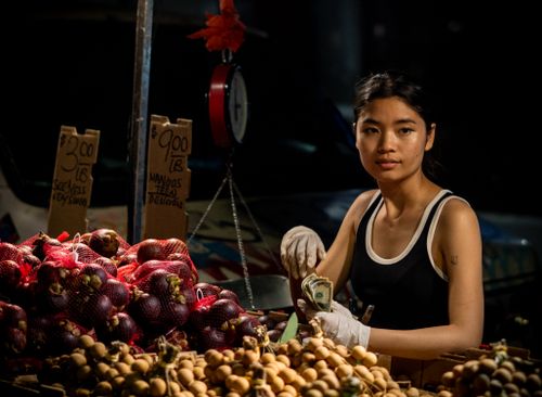 Free A young woman selling fresh produce at a night street market, handling money with a smile. Stock Photo