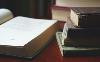 Open book beside a stack of worn hardbacks on a desk — photo by Suzy Hazelwood on Pexels