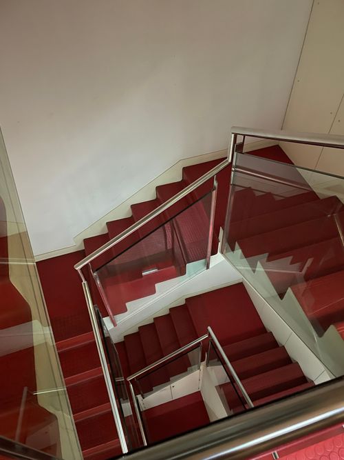 Free A high-angle view of a modern red-carpeted staircase, sleek metal handrails, and white walls. Stock Photo