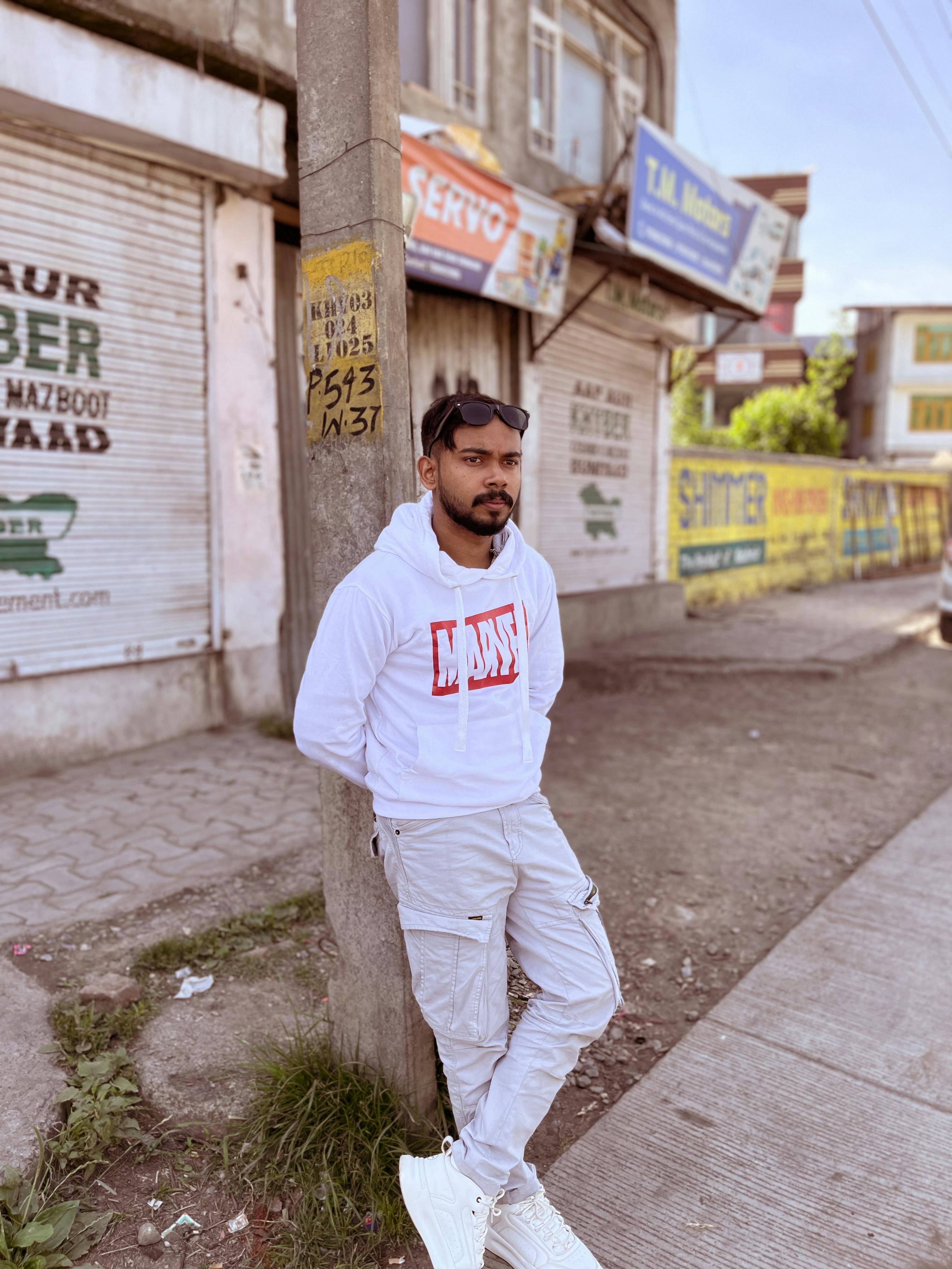 Portrait of a fashionable man in sunglasses and white hoodie standing on a city sidewalk.
