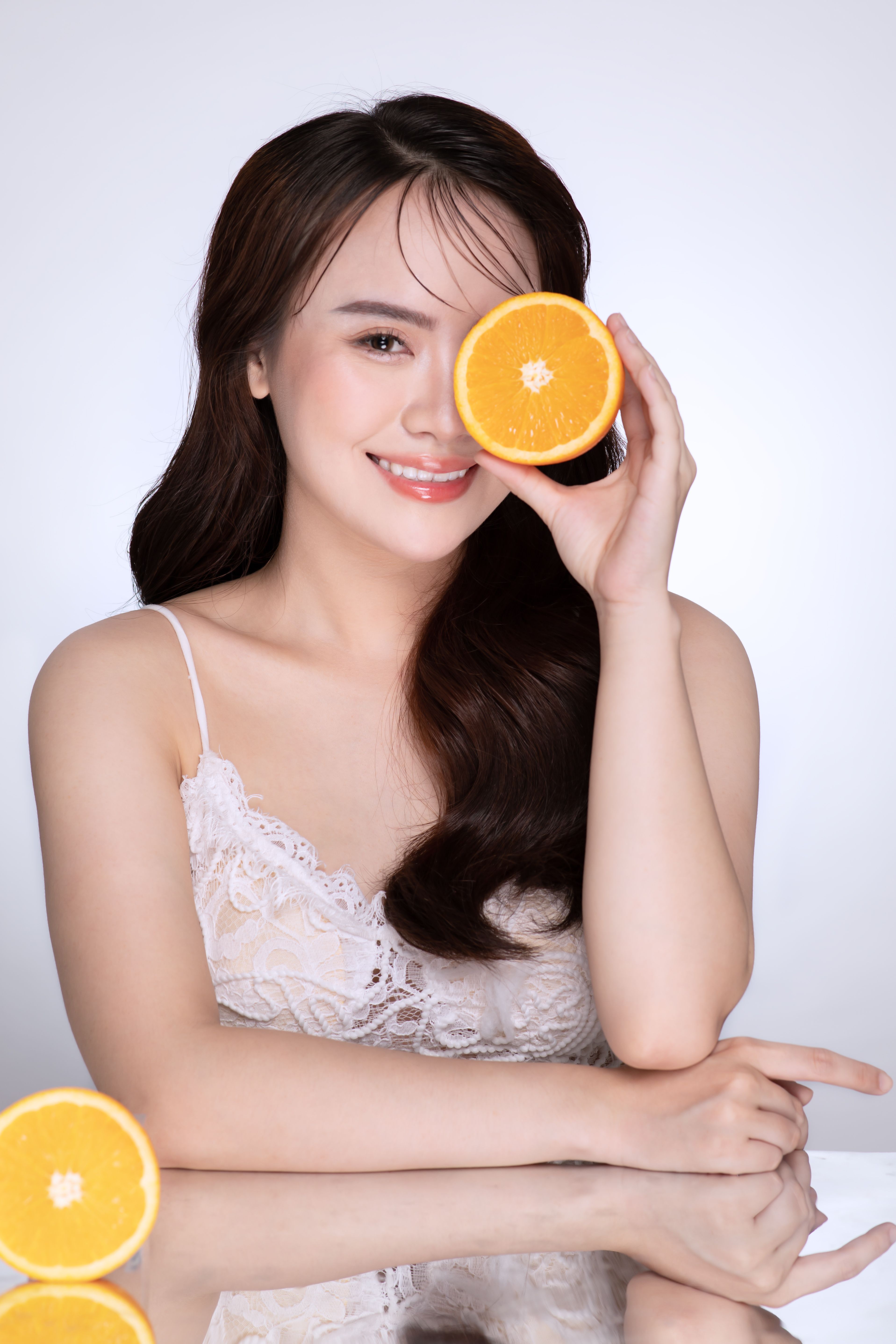 Cheerful woman holding an orange slice in a bright studio setup, highlighting freshness and health.