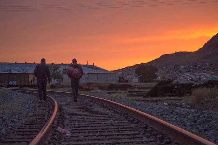 Men Walking On Railway Track At Sunset