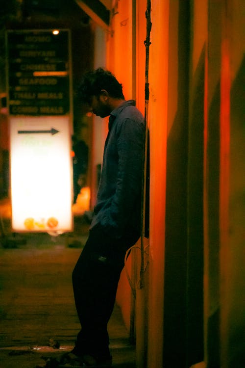 Man in Shirt Leaning Against Wall with Hands in Pockets