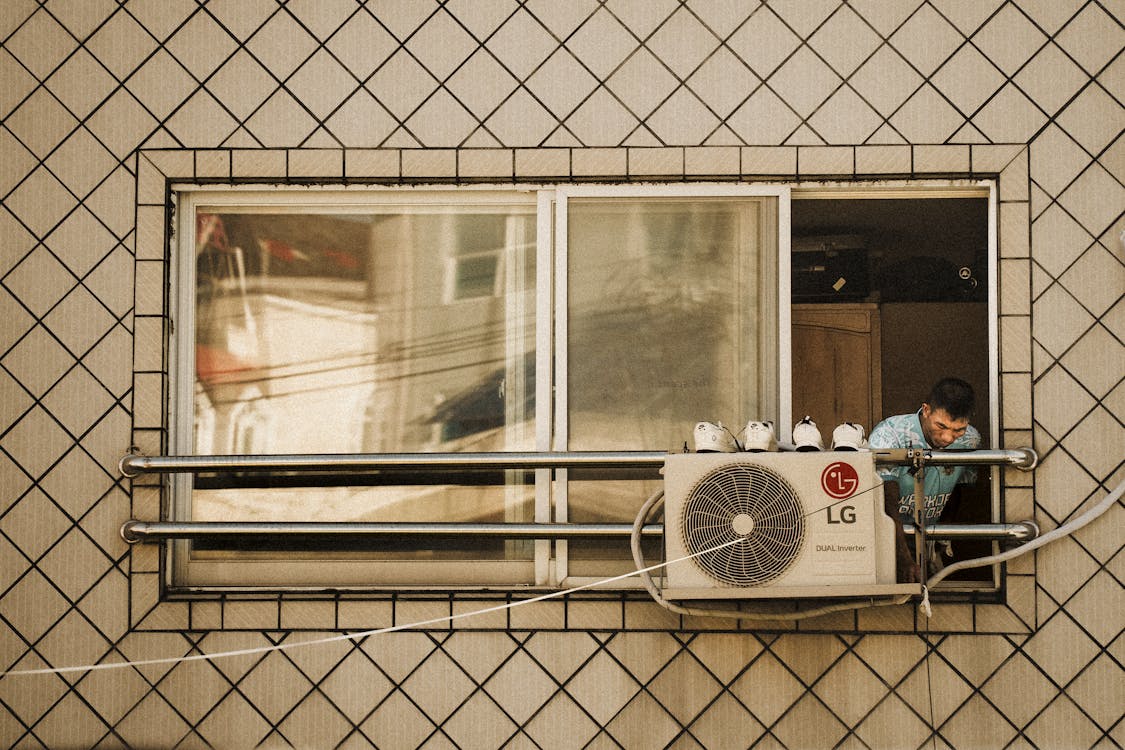 Free Man looks outside a window with an LG air conditioner unit visible, creating a reflective effect. Stock Photo