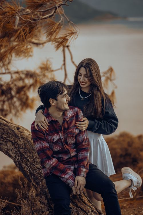 Free A young couple enjoys a tender moment on a tree trunk against a scenic outdoor backdrop. Stock Photo
