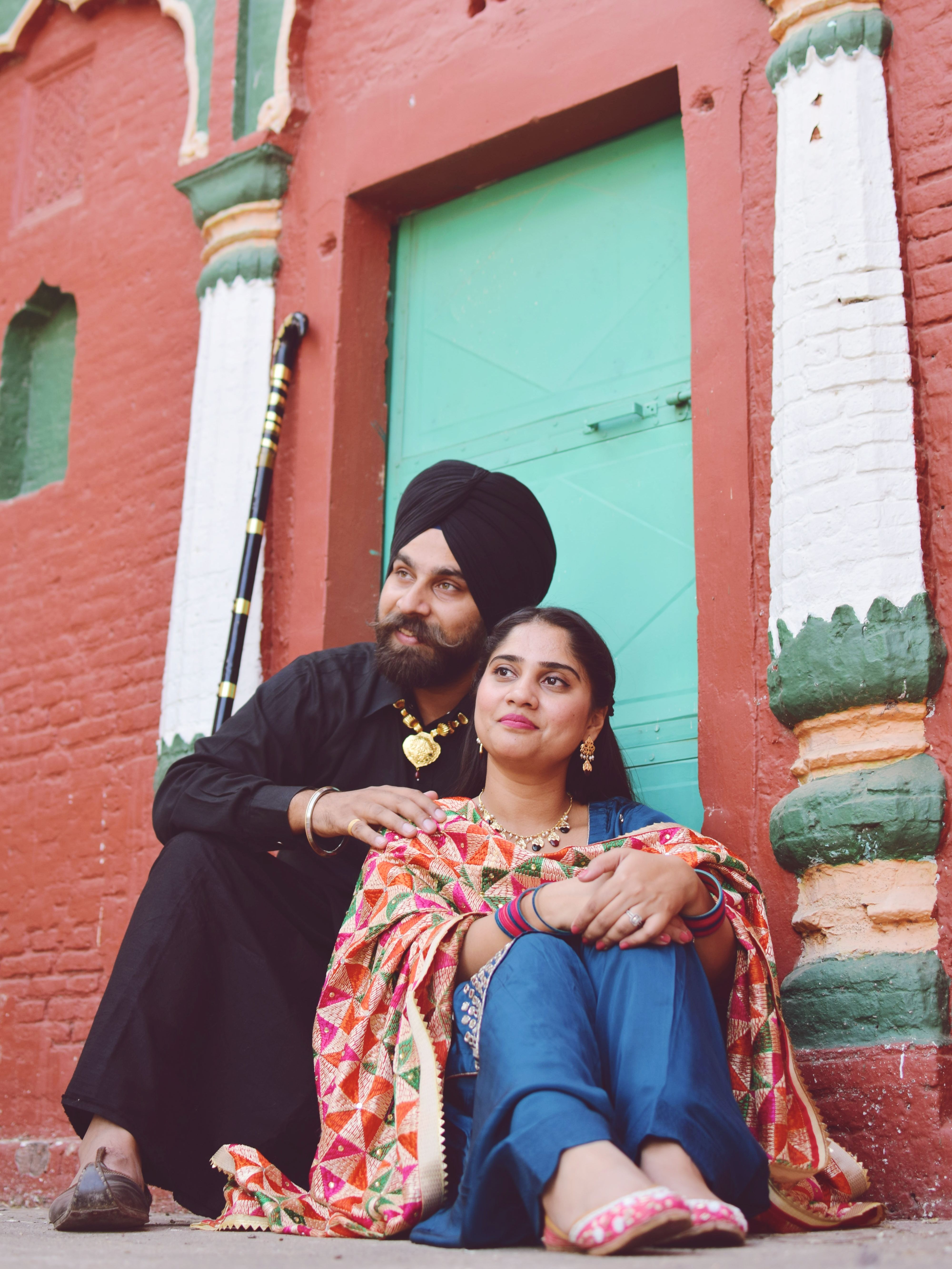 A joyful Indian couple in vibrant traditional clothing sitting together outside a colorful building.