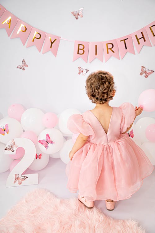 Cute Little Girl in Pink Dress Looking at Birthday Balloons