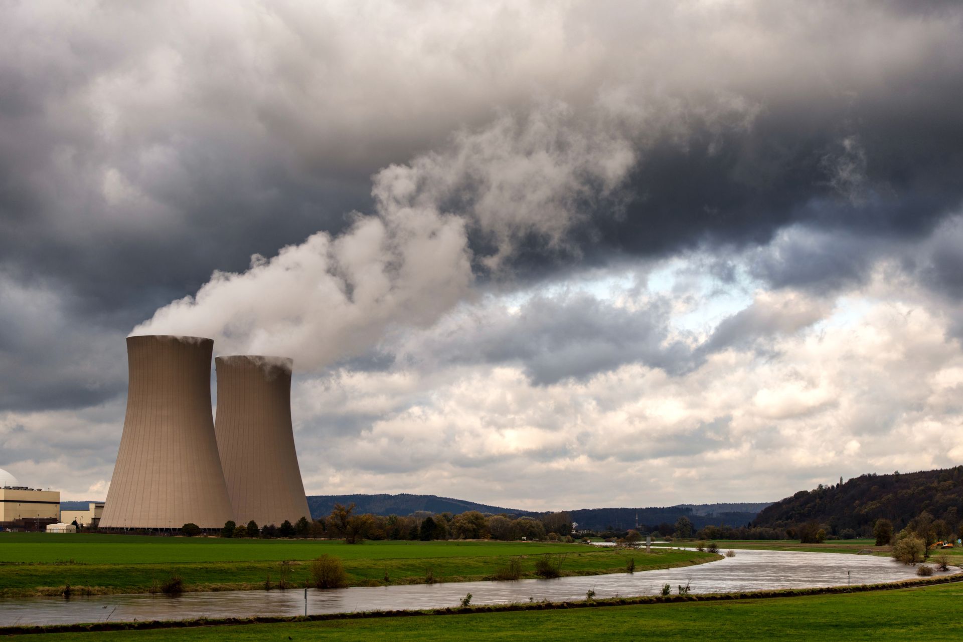 Cooling towers emit steam over a river in Hameln, Germany, under cloudy skies.