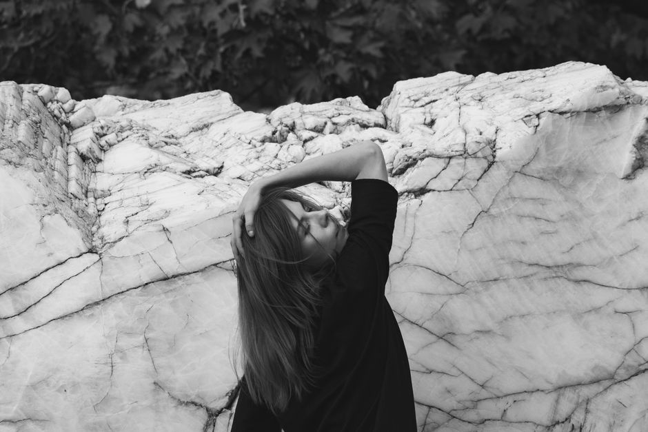 Stylish woman with brunette hair posing beside a textured marble wall. Black and white fashion portrait.