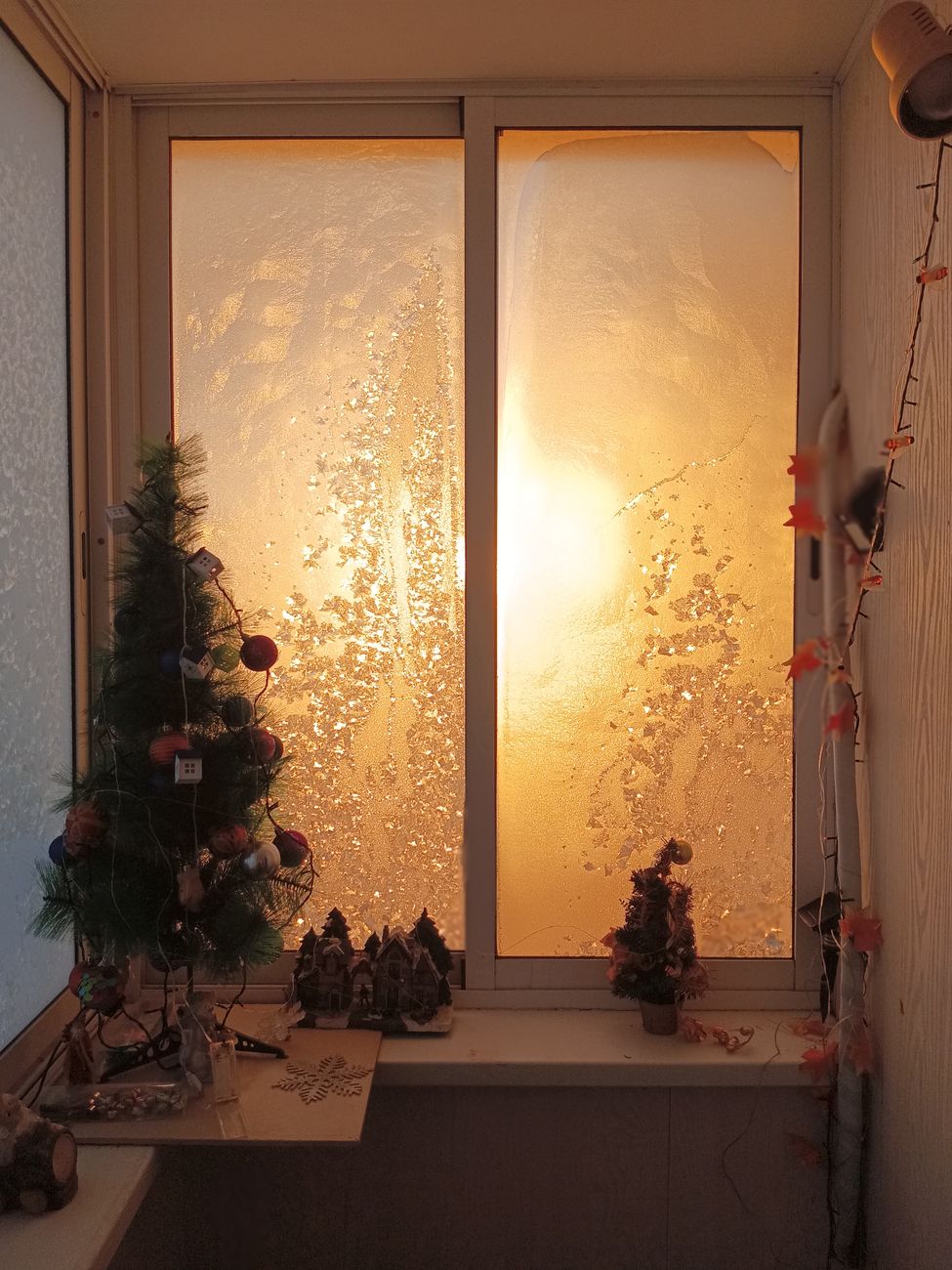 A frosty window with a small Christmas tree and decorations, captured at sunset.