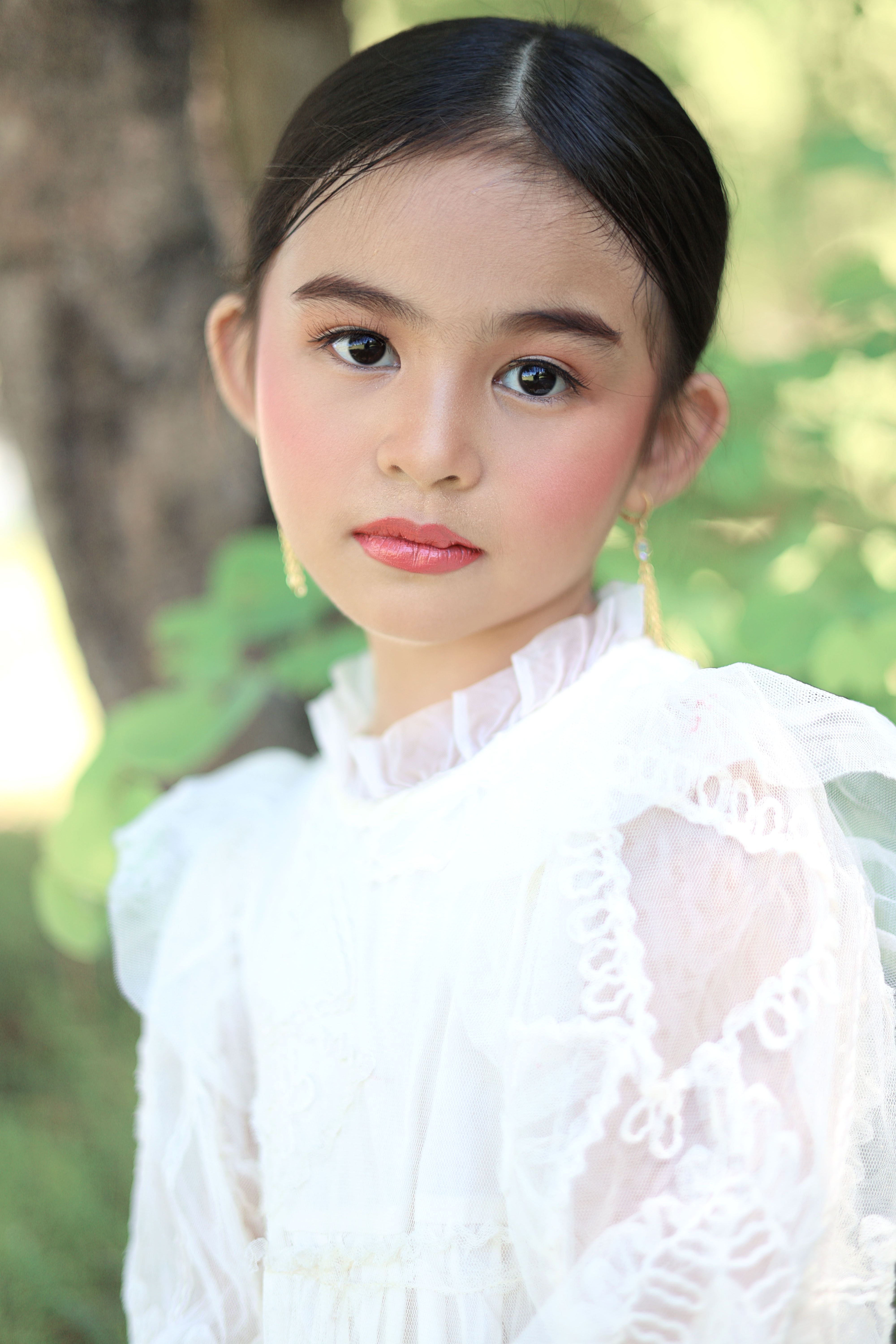 Charming portrait of a young girl in a white lace dress outdoors.