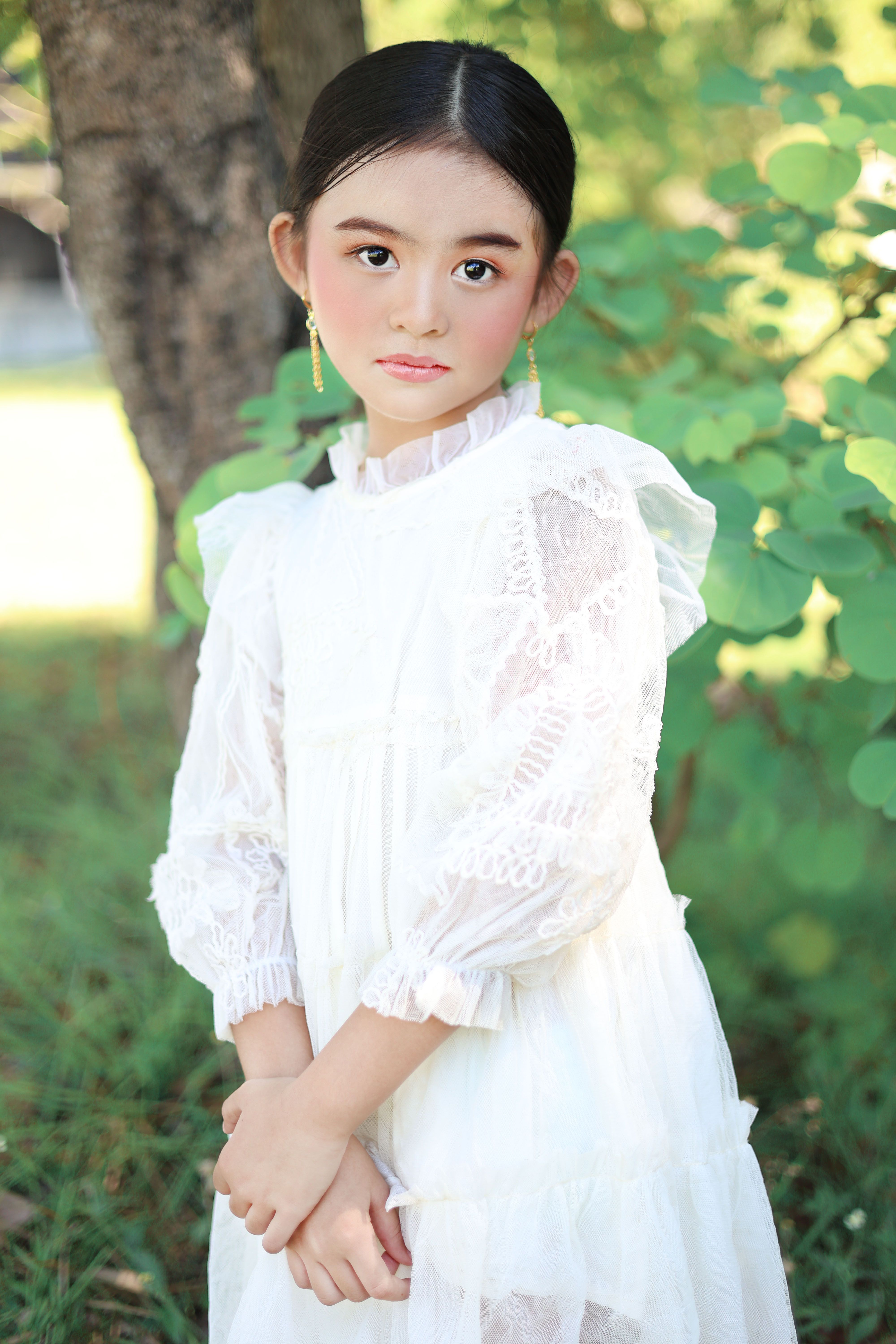 Charming portrait of a young girl in a white lace dress outdoors, exuding grace and innocence.