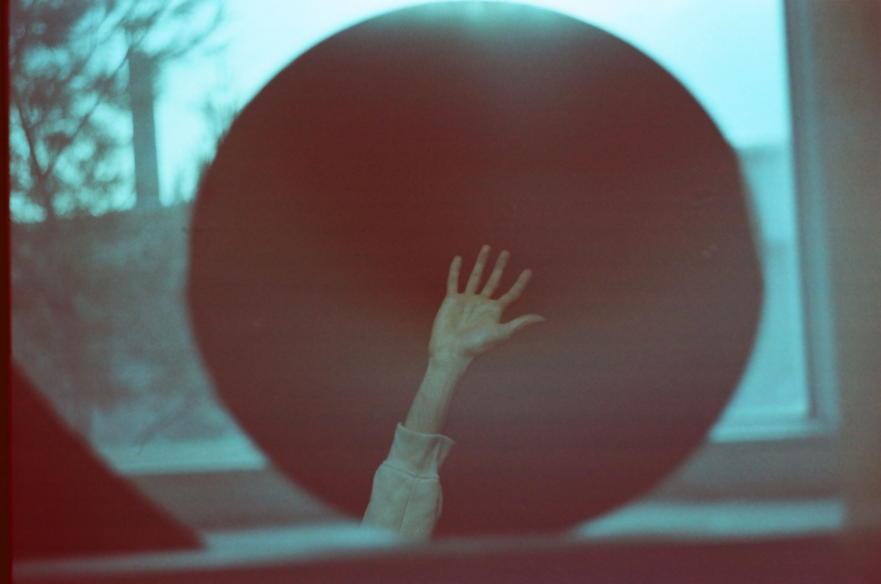 An artistic image featuring a hand raised against a circular reflective surface, captured with film photography.
