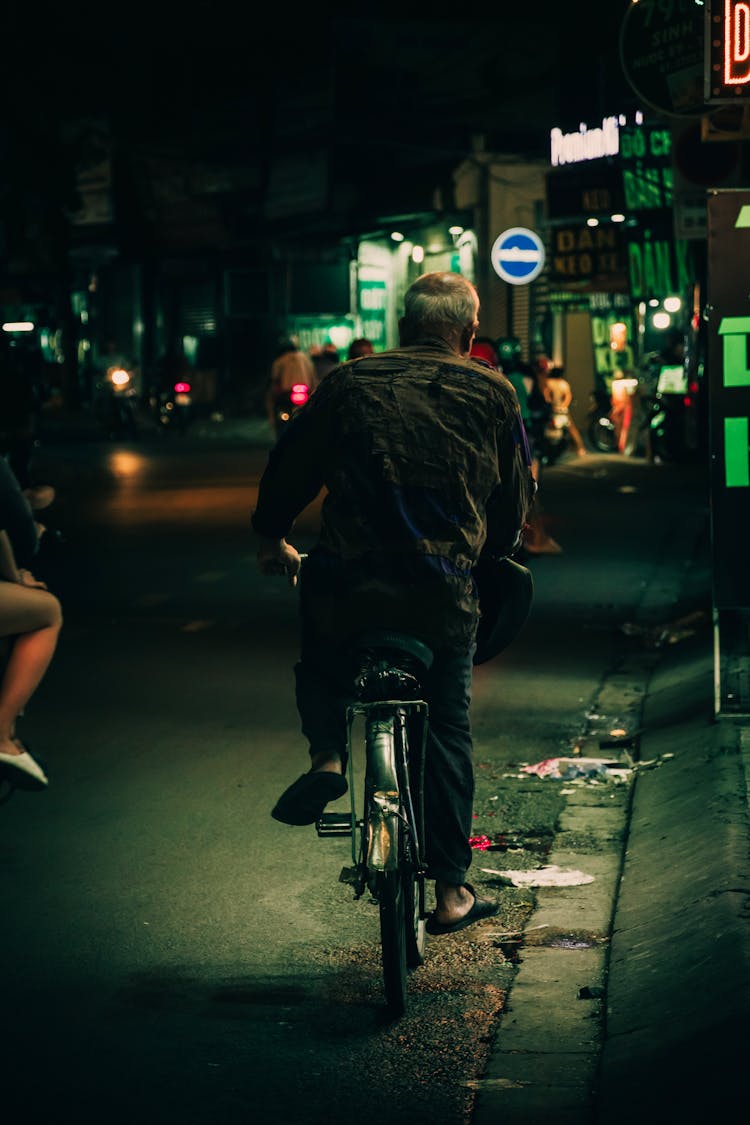 Elderly Man Riding A Bike On A Street At Night 