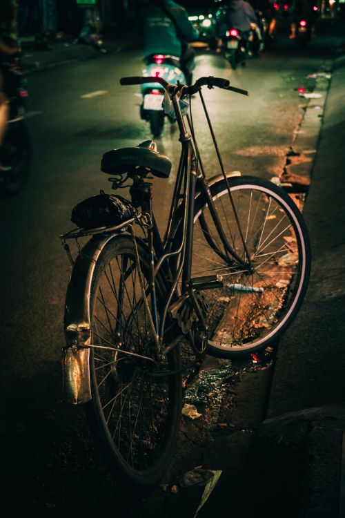 Free A vintage bicycle parked on a dimly lit urban street at night, capturing the street's ambient glow and quiet atmosphere. Stock Photo