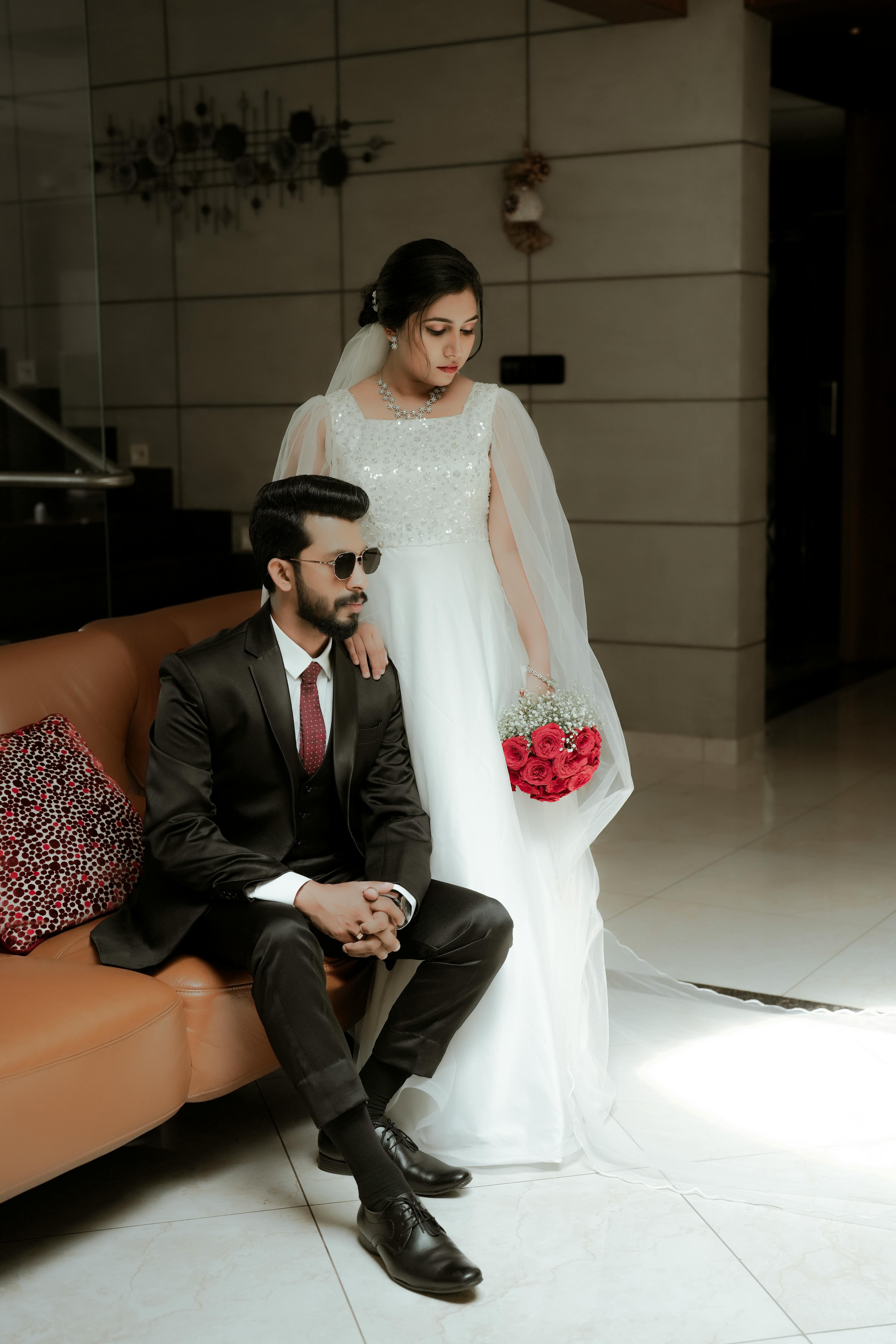 free photo of groom sitting on a couch and the bride standing beside