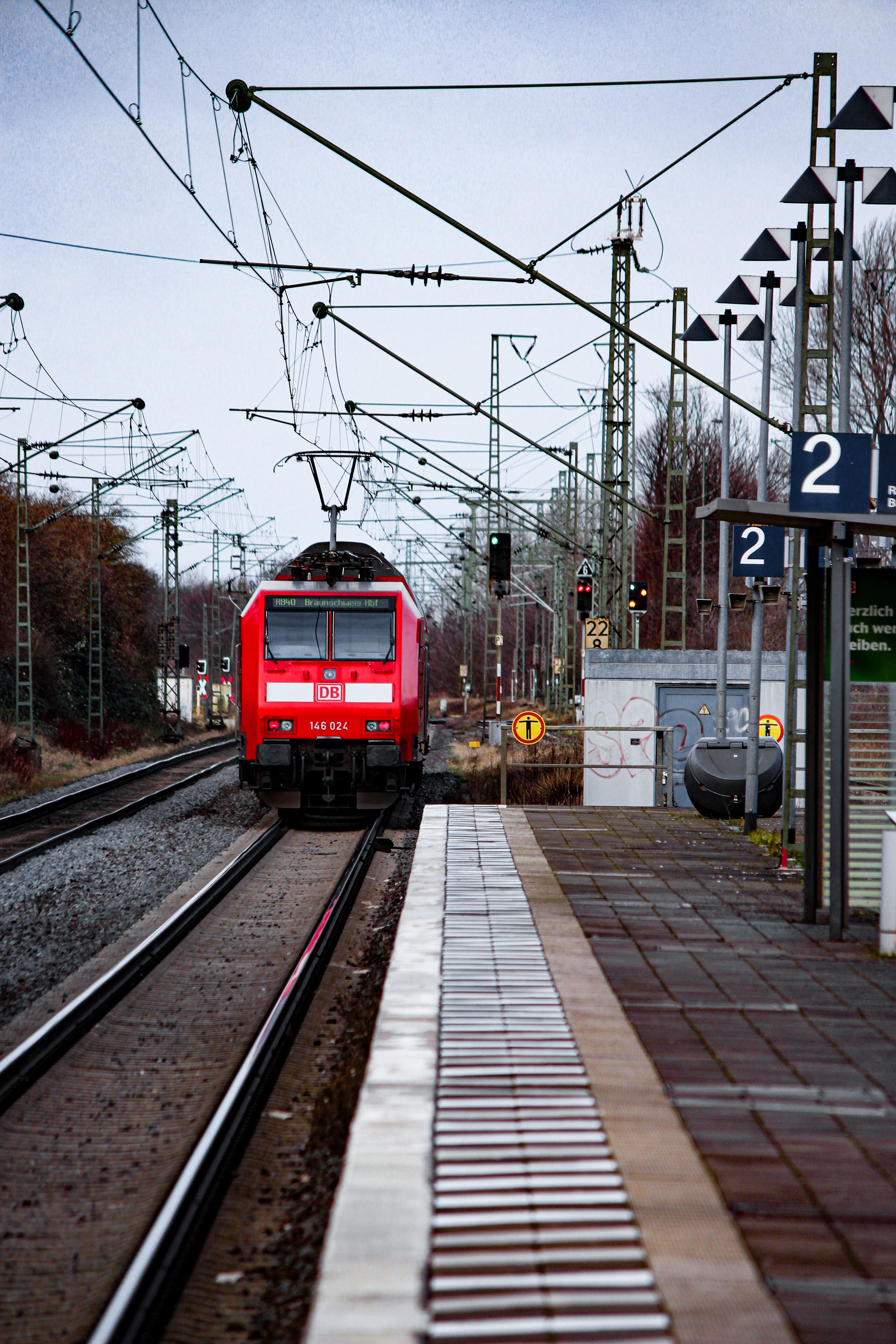 A vibrant red train approaches a station platform under an overcast sky in Europe.