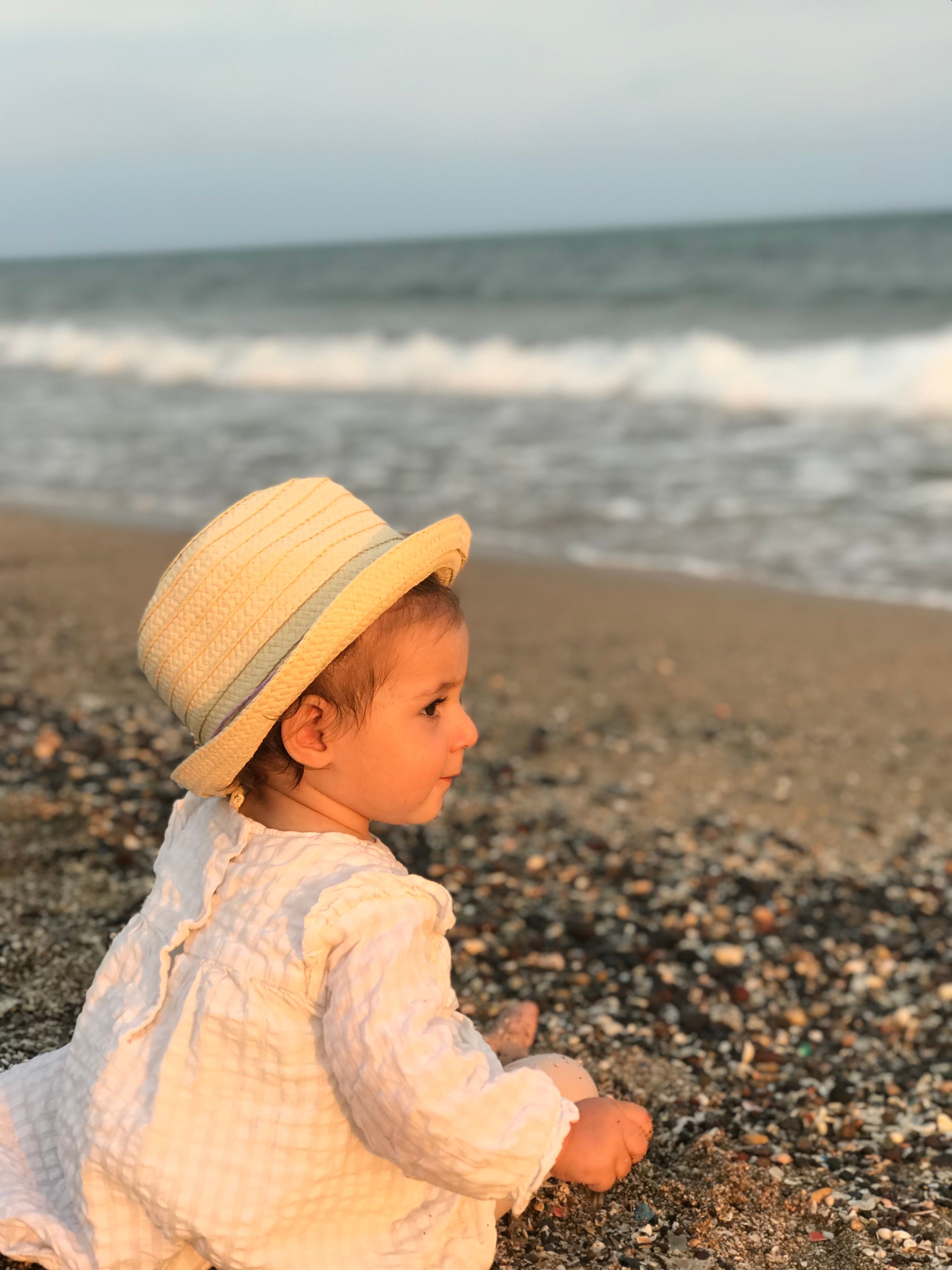 Bébé coiffé d’un chapeau assis sur le sable face à la mer