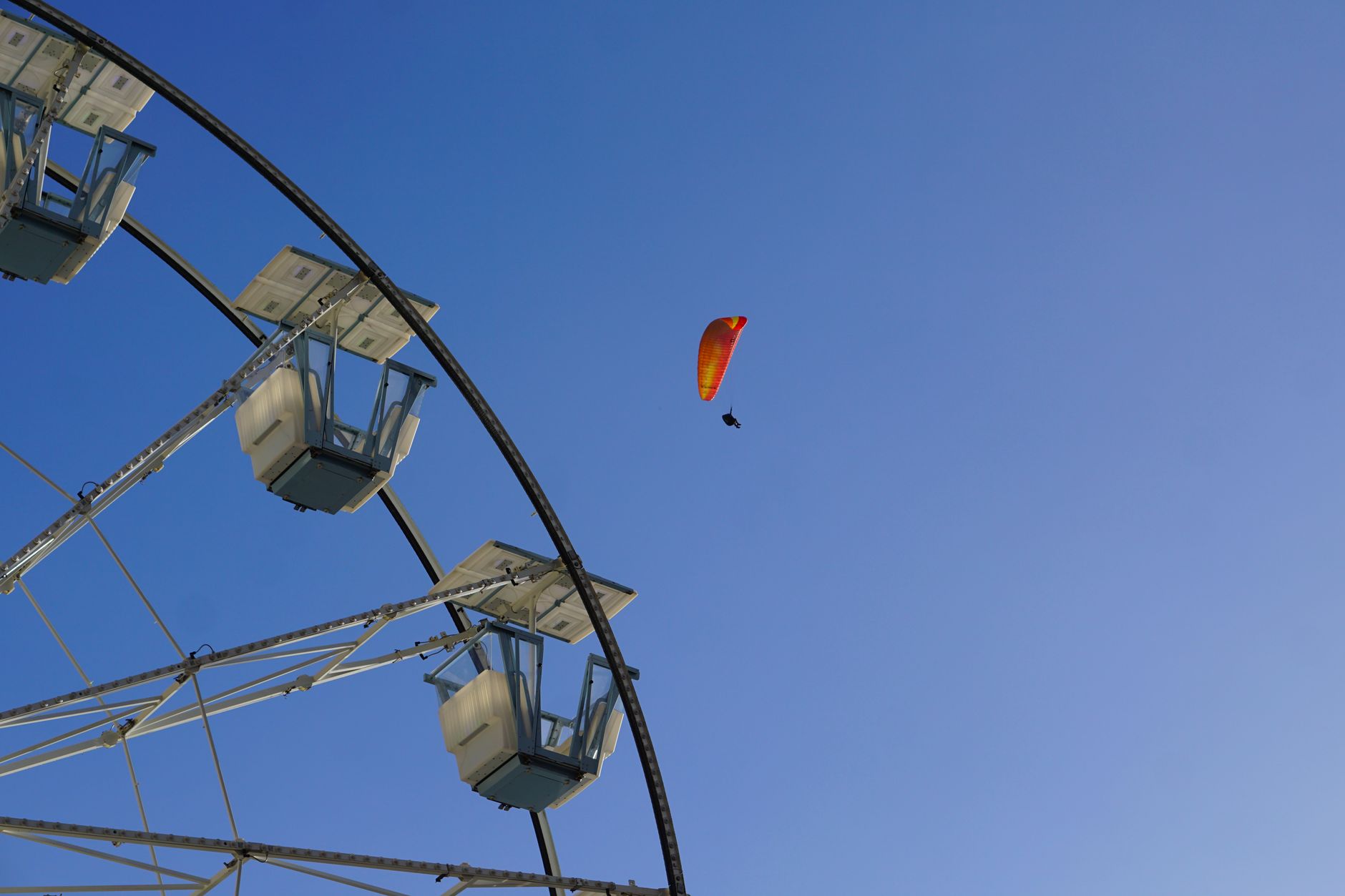 A paraglider soaring high in the sky above a Ferris Wheel on a clear day.