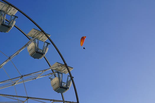A paraglider soaring high in the sky above a Ferris Wheel on a clear day.