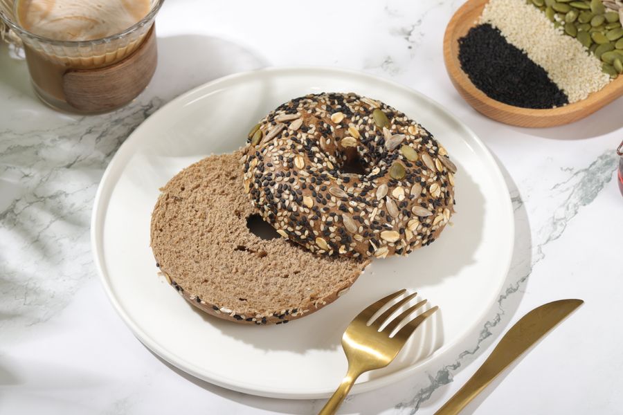 Delicious multigrain bagel with seeds on a plate, next to a creamy latte.