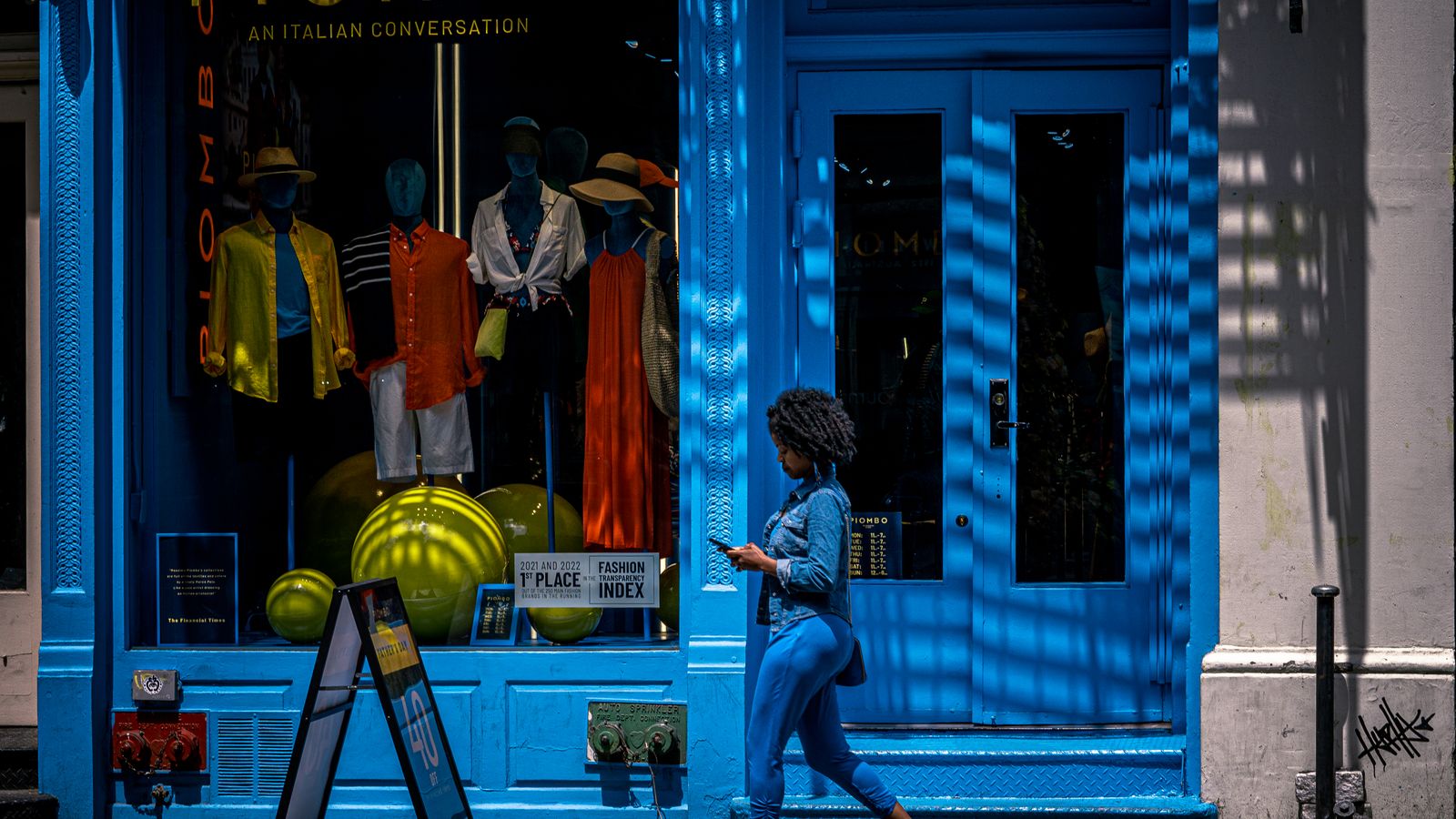A woman with a smartphone passes a stylish clothing store in New York City.