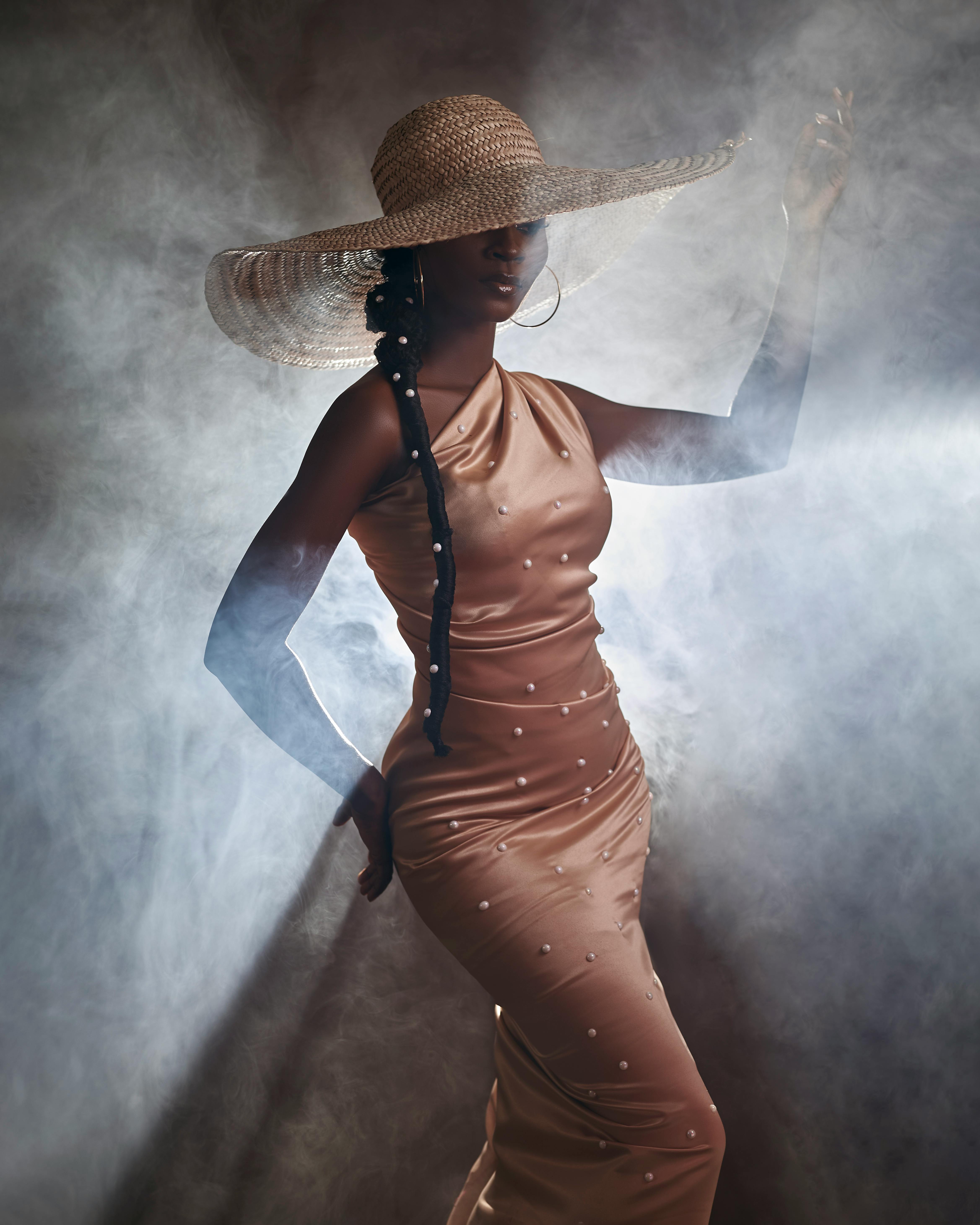 Stunning portrait of a woman in a glamorous dress and hat, posing in a smoky studio setting.
