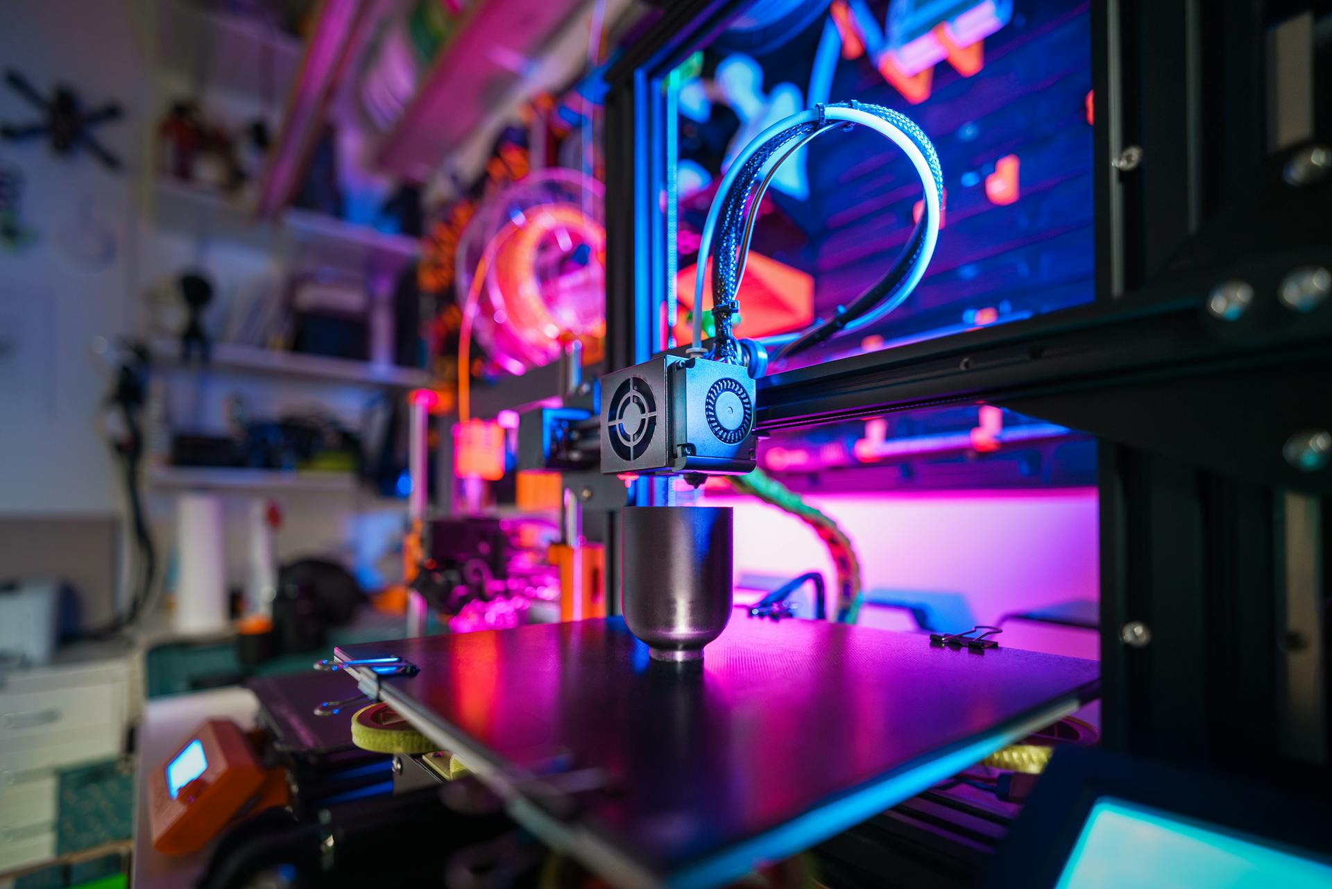 A close-up of a modern 3D printer in action, illuminated by vibrant, colorful lighting indoors.