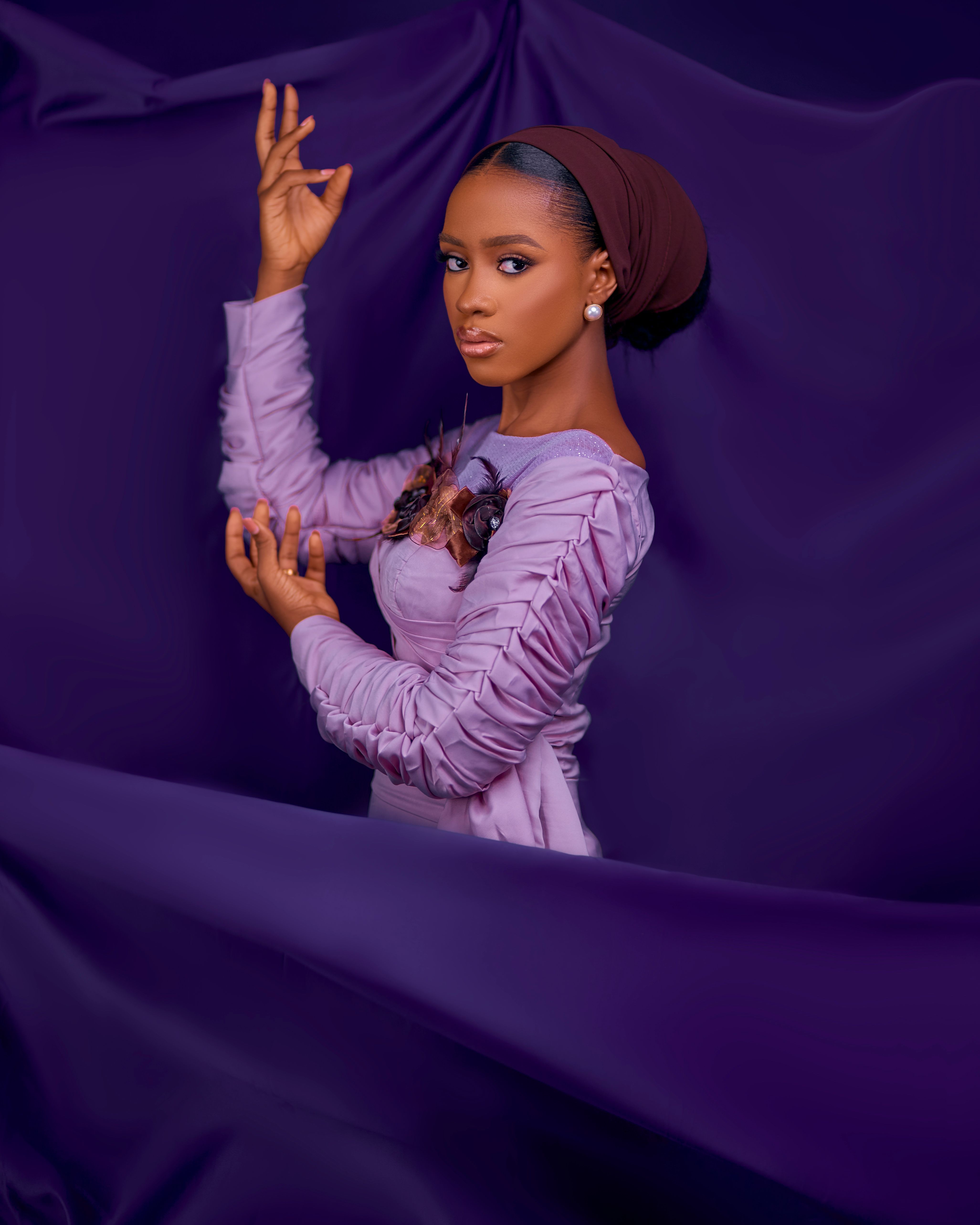 Striking studio fashion portrait of a woman in a purple dress and headscarf posing gracefully.
