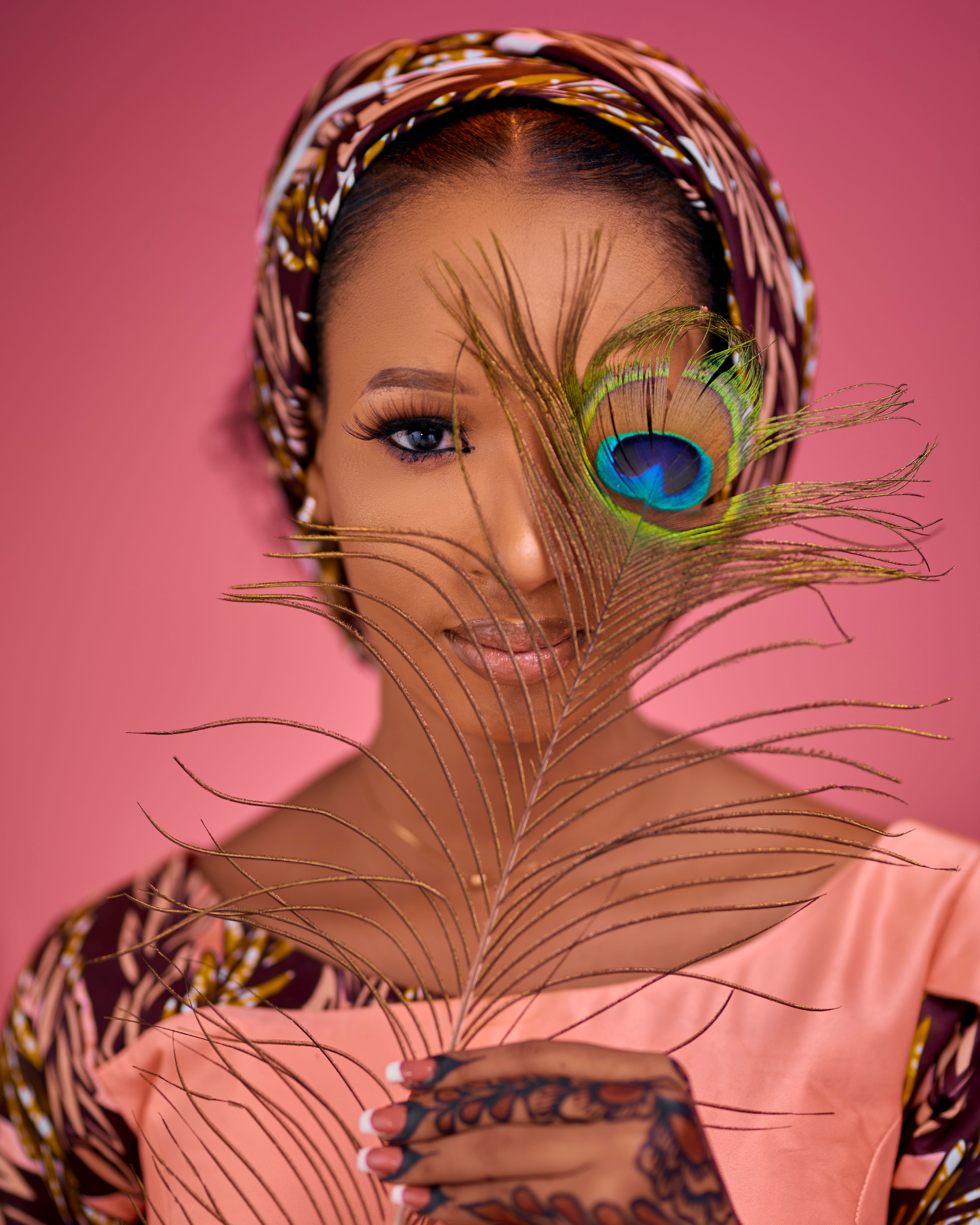 Elegant portrait of a woman holding a peacock feather with vibrant colors and a patterned headscarf.