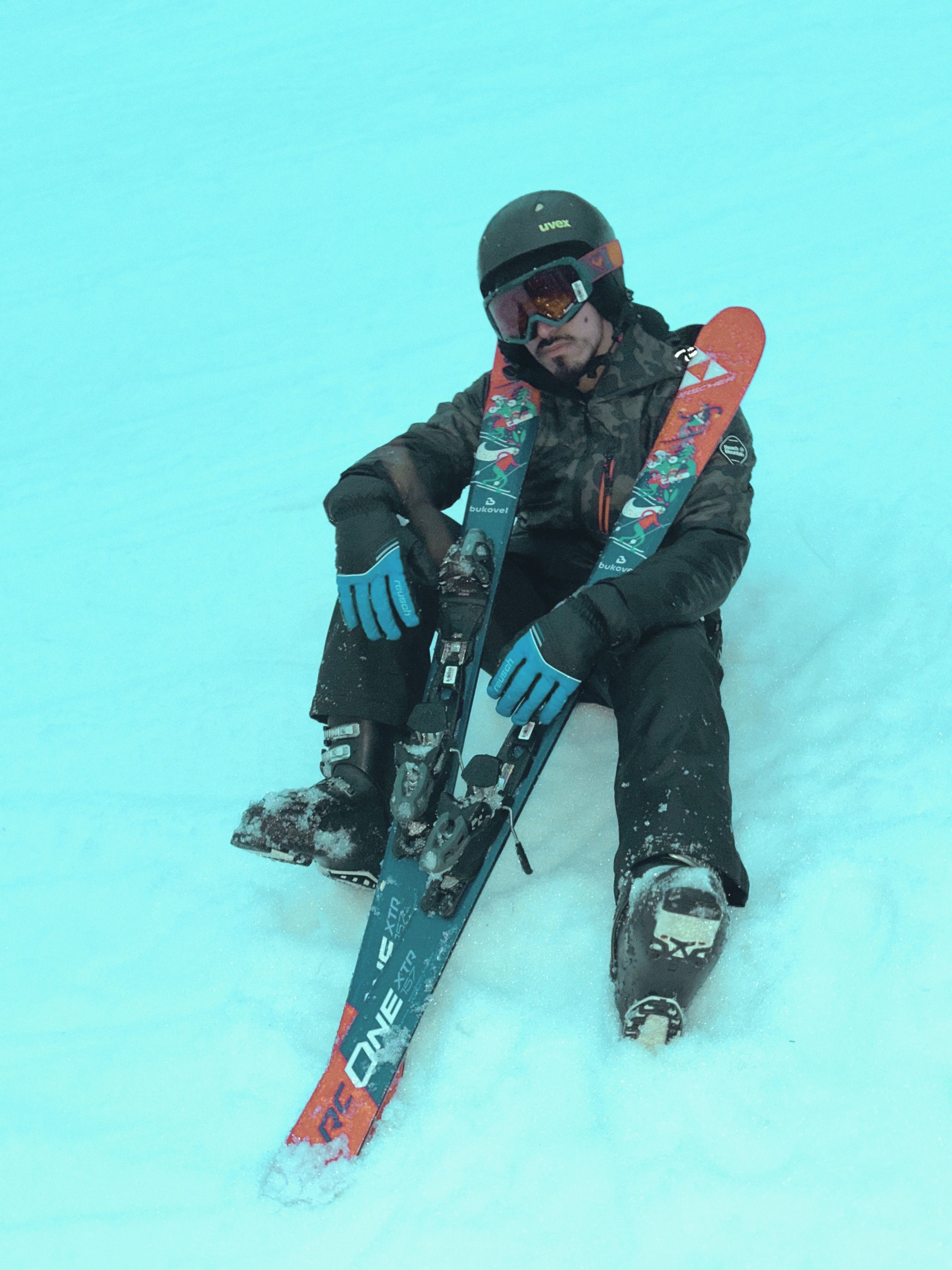 Man sitting on snow with skis, wearing a helmet and goggles in winter.