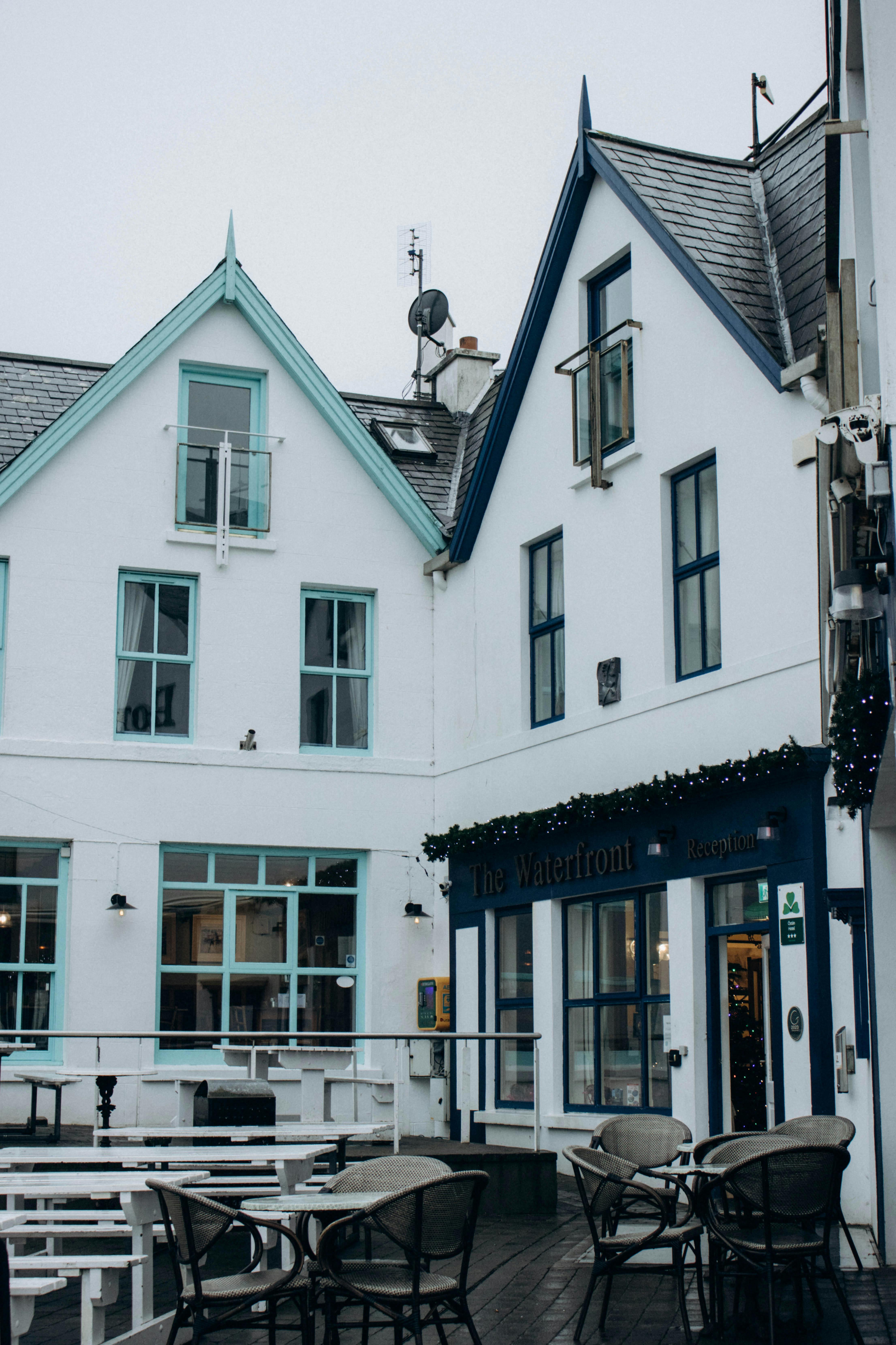Cozy outdoor cafe with white buildings and teal accents on a cloudy day, perfect for relaxation.