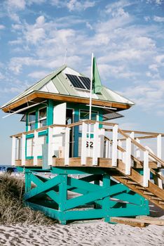 A colorful lifeguard tower stands on a sandy beach under a blue sky with clouds.