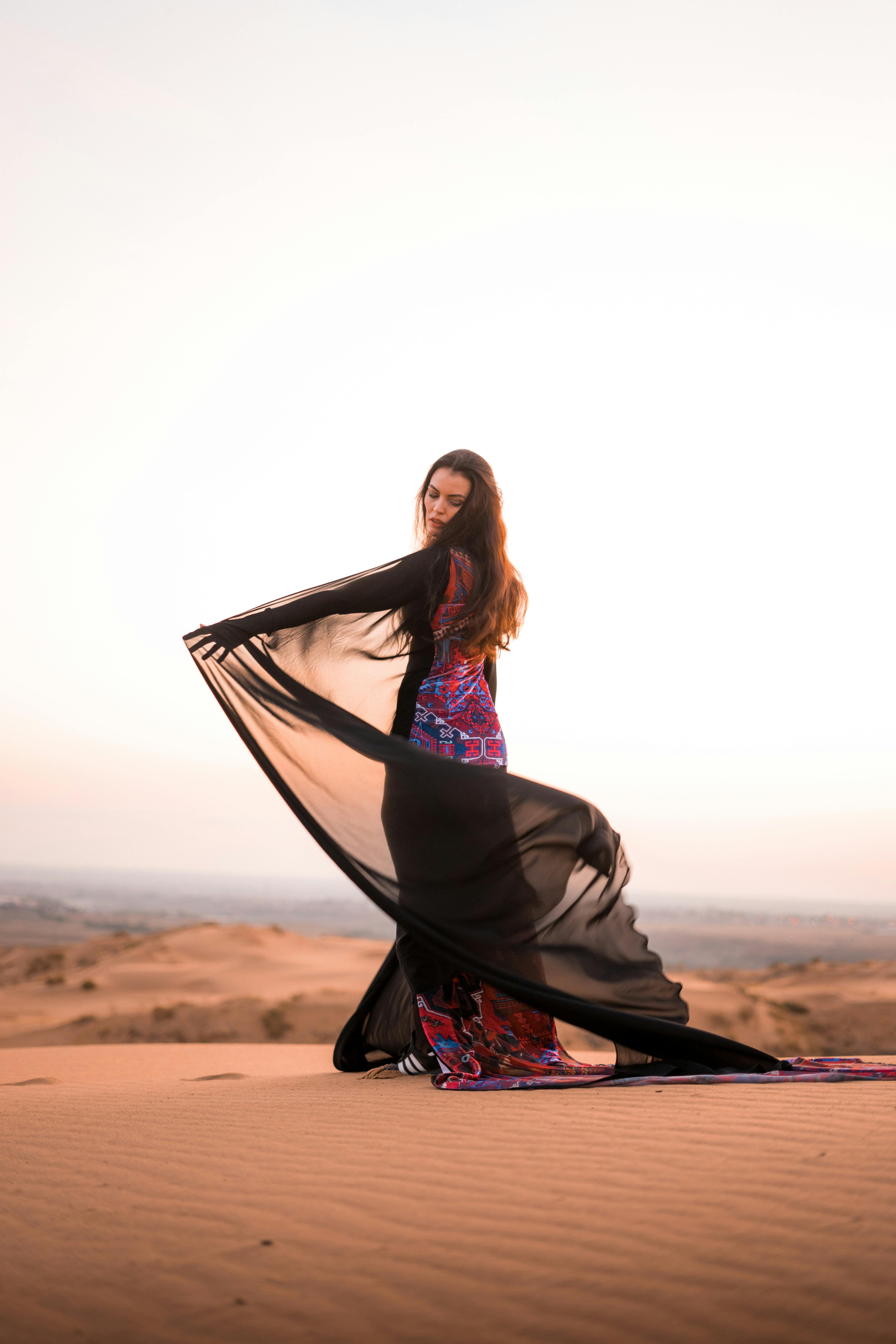 Woman in bedouin clothes standing on dune in desert Stock Photo