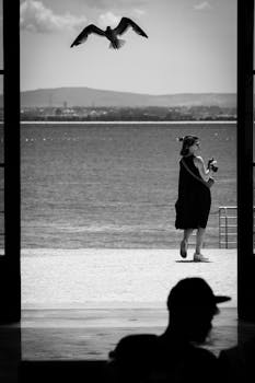 Captivating black and white image of a woman and bird at the beach, perfect for travel and lifestyle themes.