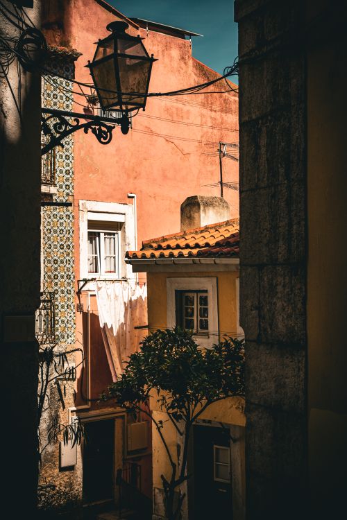 Free Sunlit alleyway featuring vintage architecture with vibrant facades and a street lamp. Stock Photo