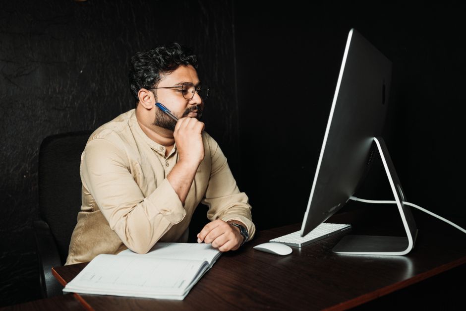 A thoughtful office worker in glasses analyzes information on a computer screen, pen in hand.