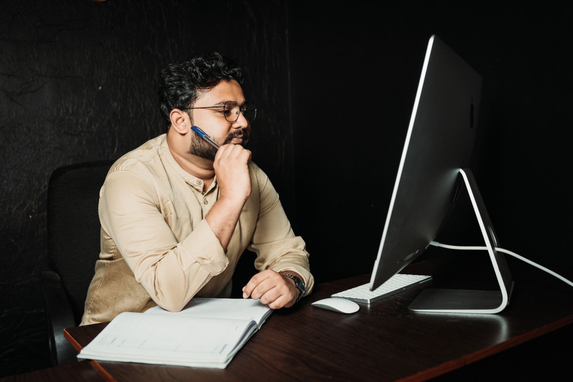A thoughtful office worker in glasses analyzes information on a computer screen, pen in hand.