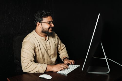 Free Adult man working on a computer at a desk in a dimly lit office environment. Stock Photo