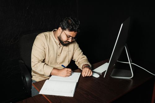 Free Man writing in office with computer. Late-night work focused on creativity and productivity. Stock Photo