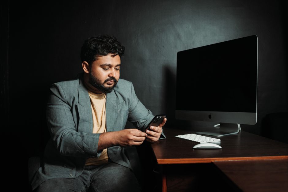 Adult man using smartphone at desk with computer in a modern office. Adult man using smartphone at desk with computer in a modern office.