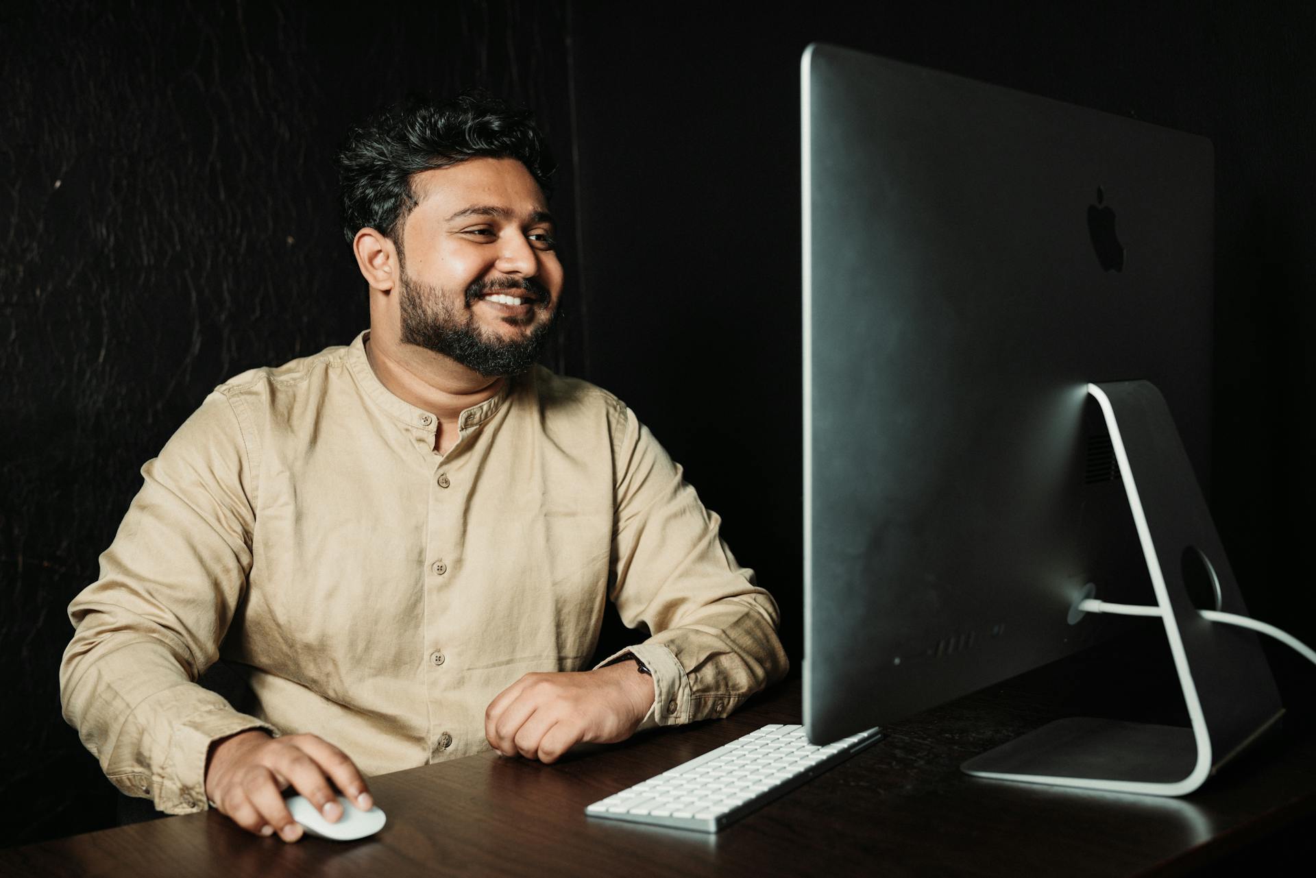 A smiling adult man using a desktop computer at a desk, creating a positive work environment.