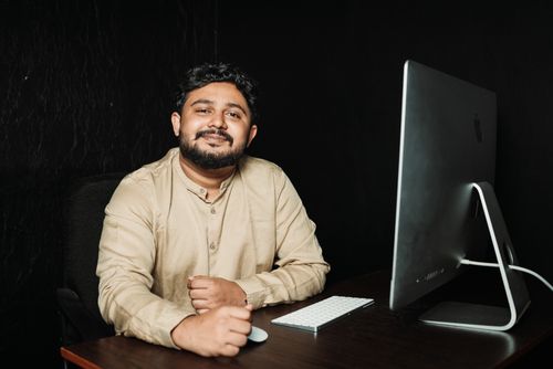 Free Smiling office worker sitting at desk with computer in a dimly lit office. Stock Photo