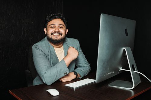 Free A professional smiling confidently at his desk with a modern computer setup. Stock Photo