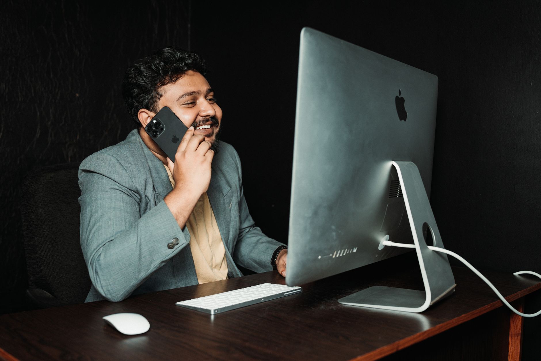 Professional man in a suit talking on phone while working at a desk with computer and accessories.