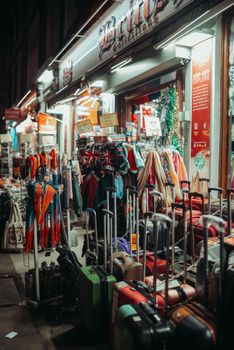 Illuminated street store showcasing merchandise with umbrellas and suitcases at night.