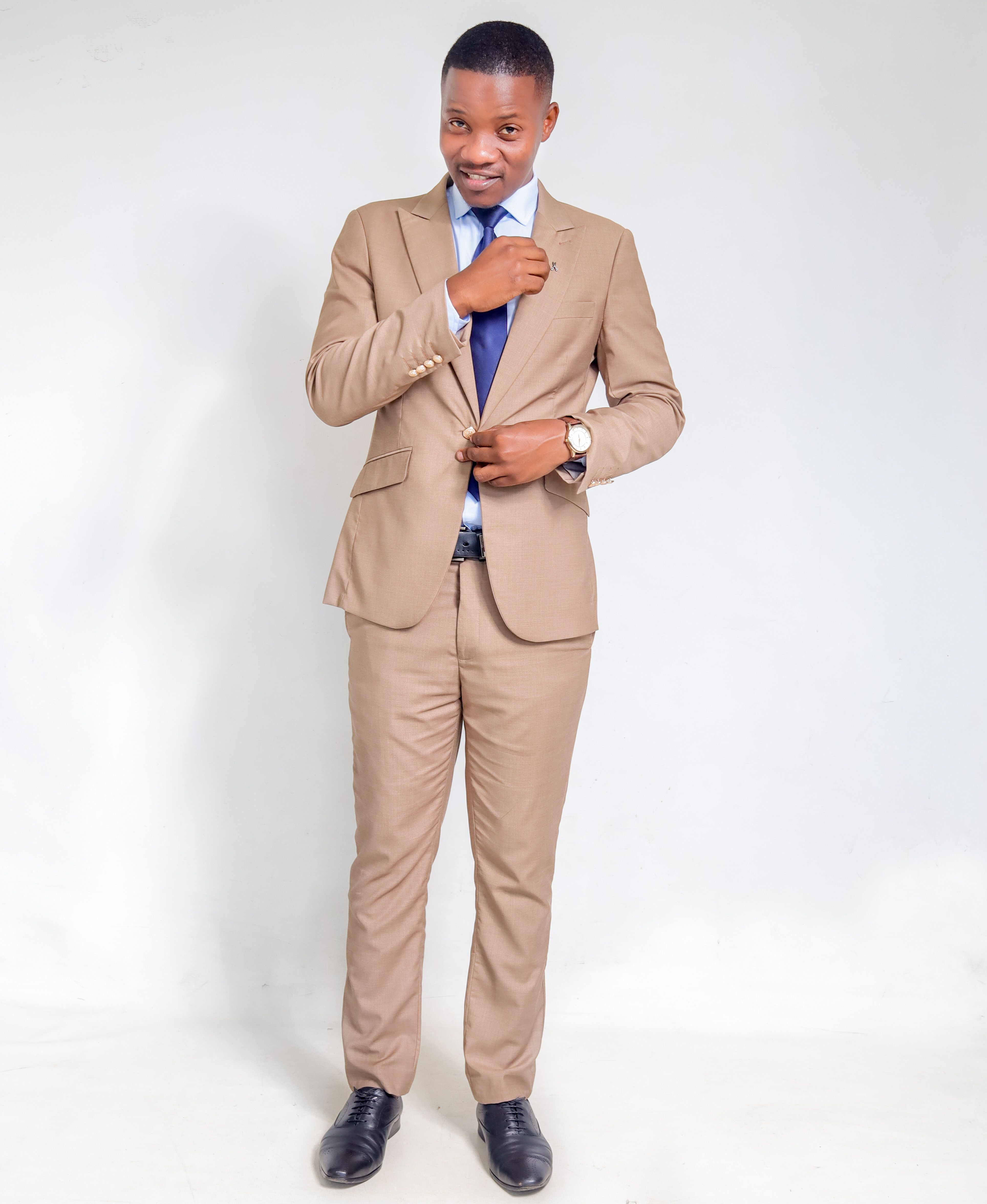 A professional man in a beige suit with a blue tie adjusts his jacket on a white background.