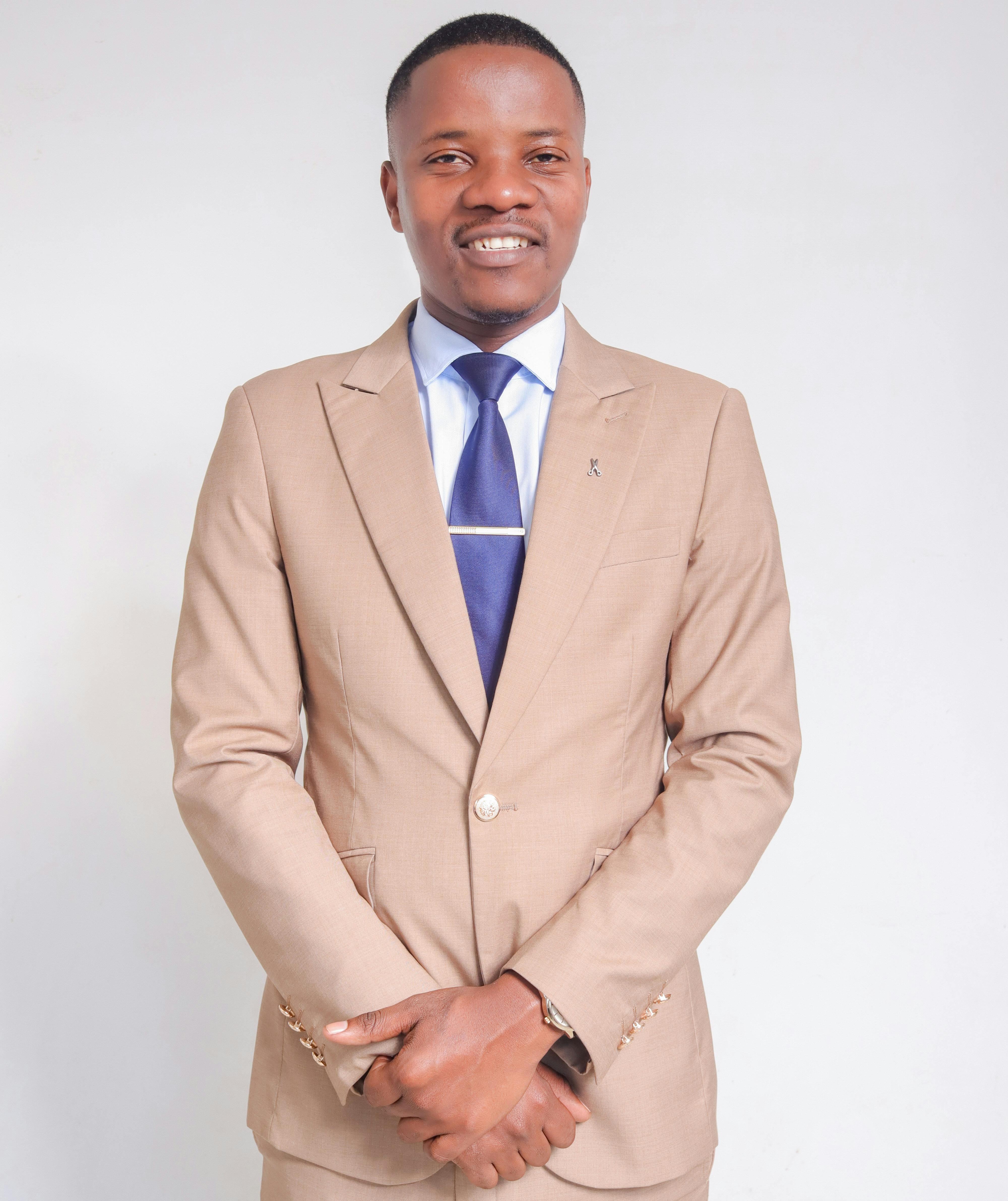Portrait of a smiling man in a beige suit and blue necktie against a neutral background.